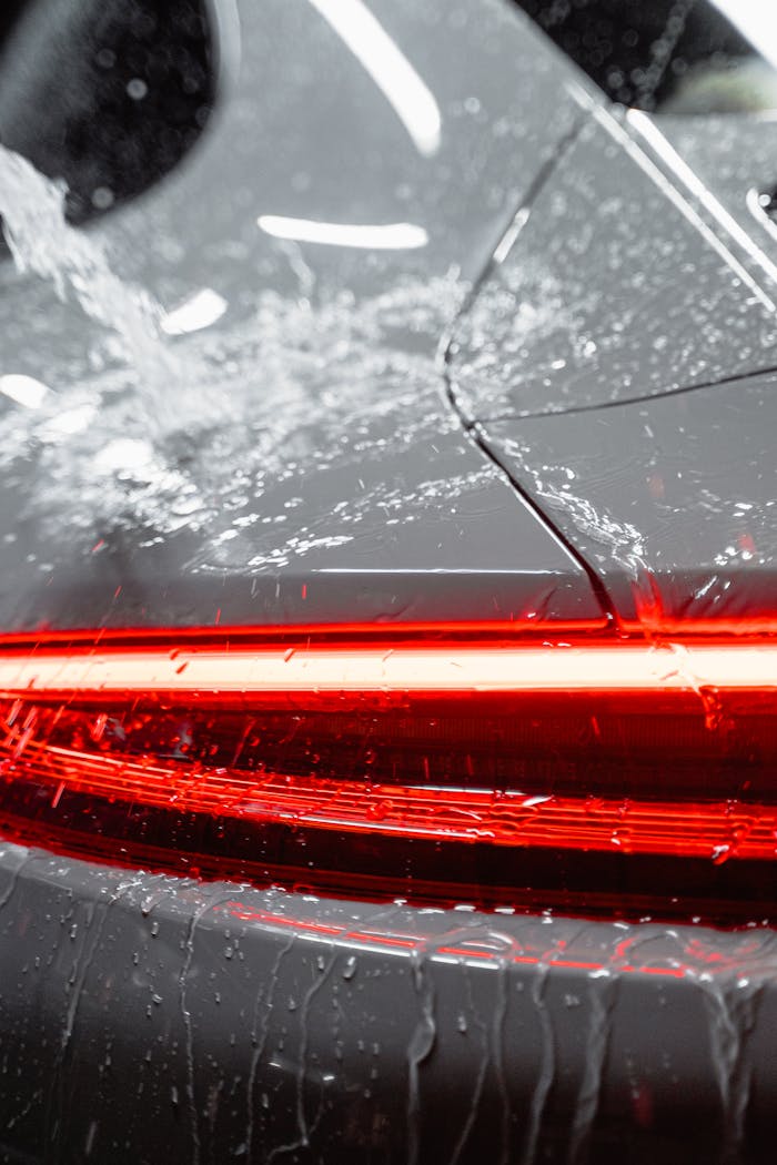 Close-up of a vehicles taillight being washed, featuring water and soap suds for a clean and shiny finish.